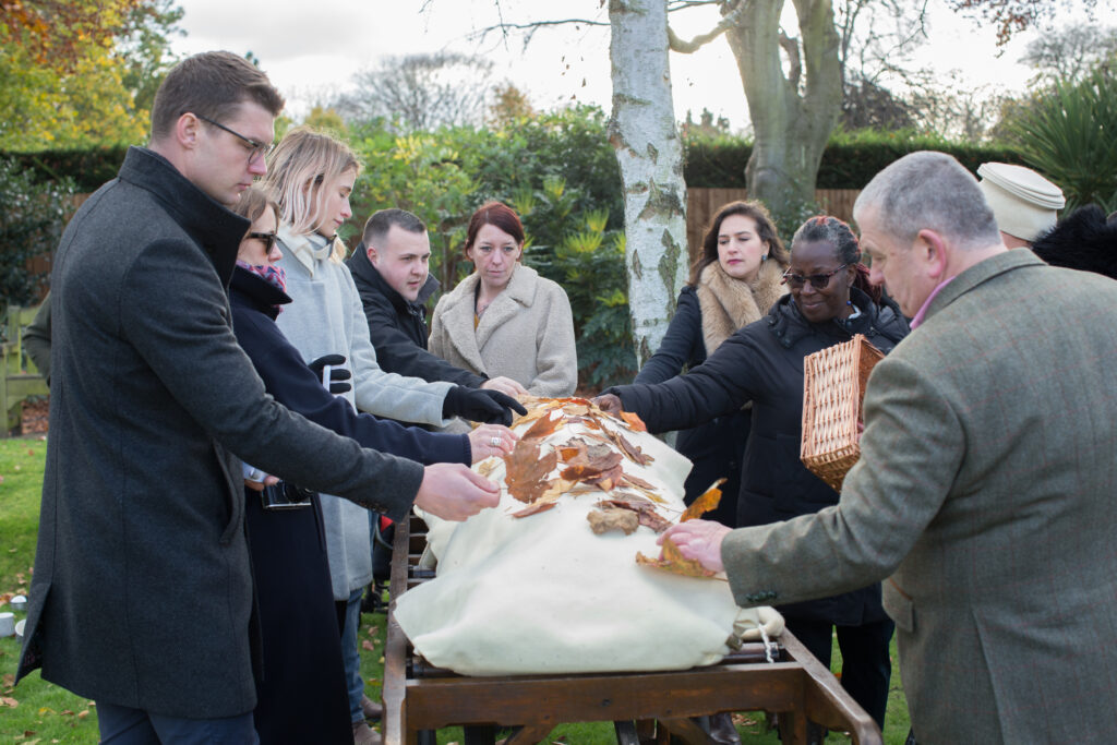 natural burial as alternative to cremation  family putting leaves on a shroud wrapped dead person
