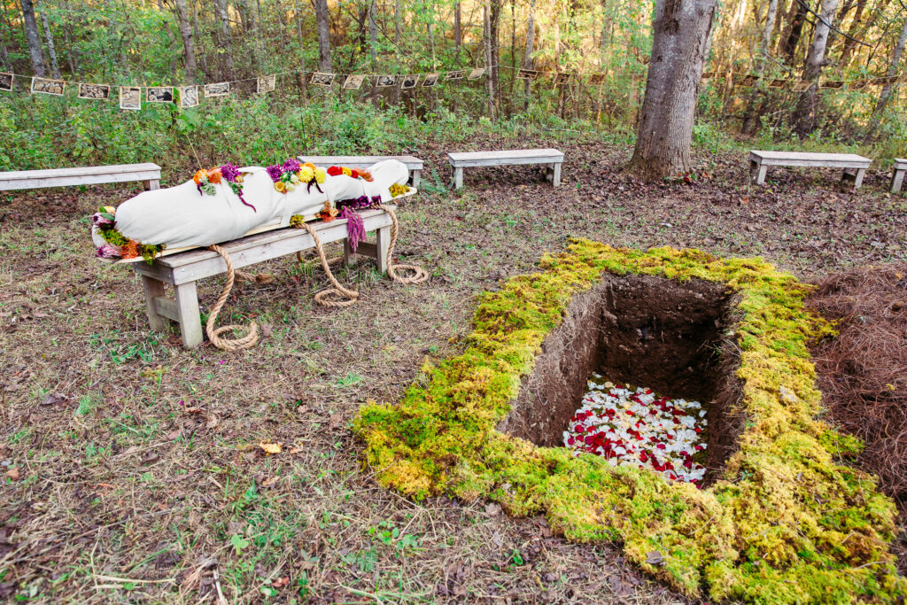 natural woodland burial as an alternative to cremation
burial plot with flowers petals and moss decorating it a dead person in a shroud covered in flowers